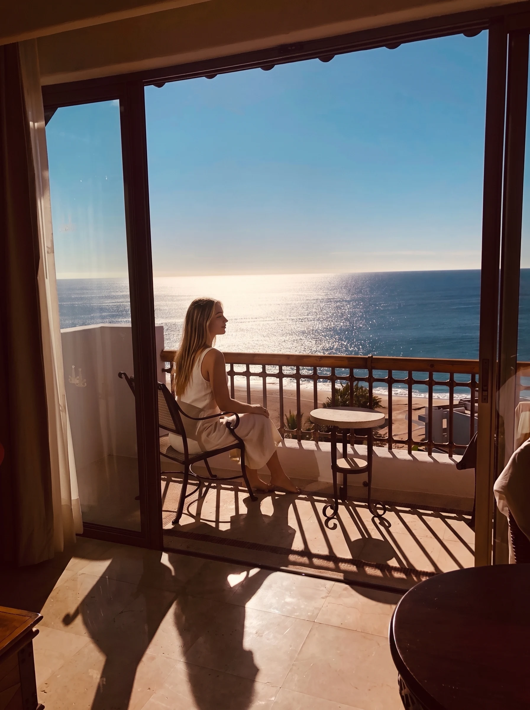 Audrey seated on the room balcony looking out at the sunlit sea.