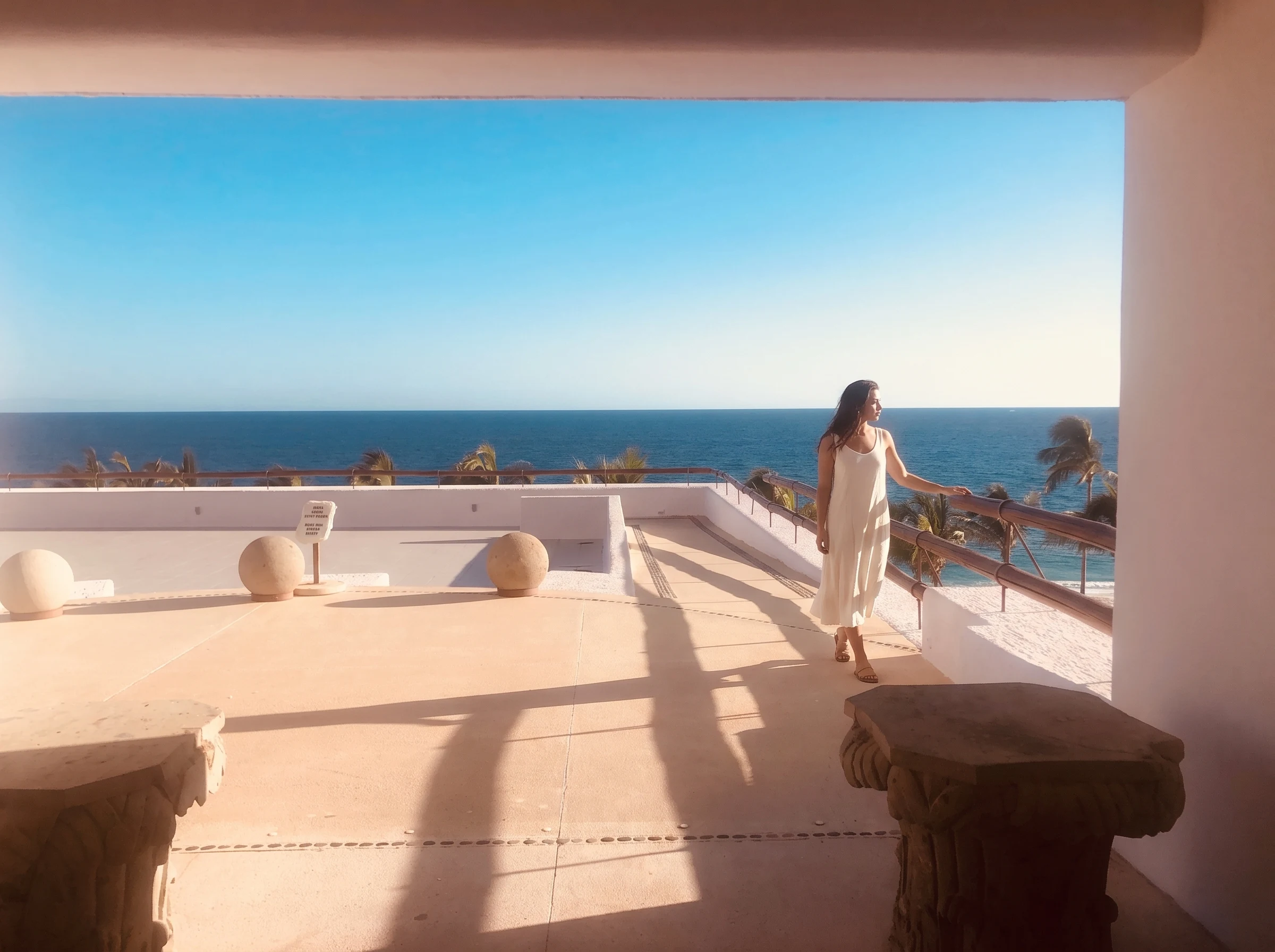 Audrey in an ivory dress on the sunlit ocean-facing terrace.