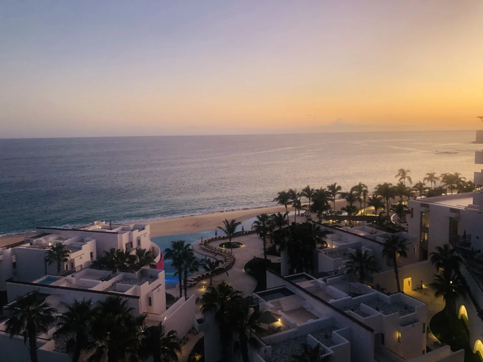 Marquis Los Cabos pools, palms and white buildings overlooking the sea at sunset.