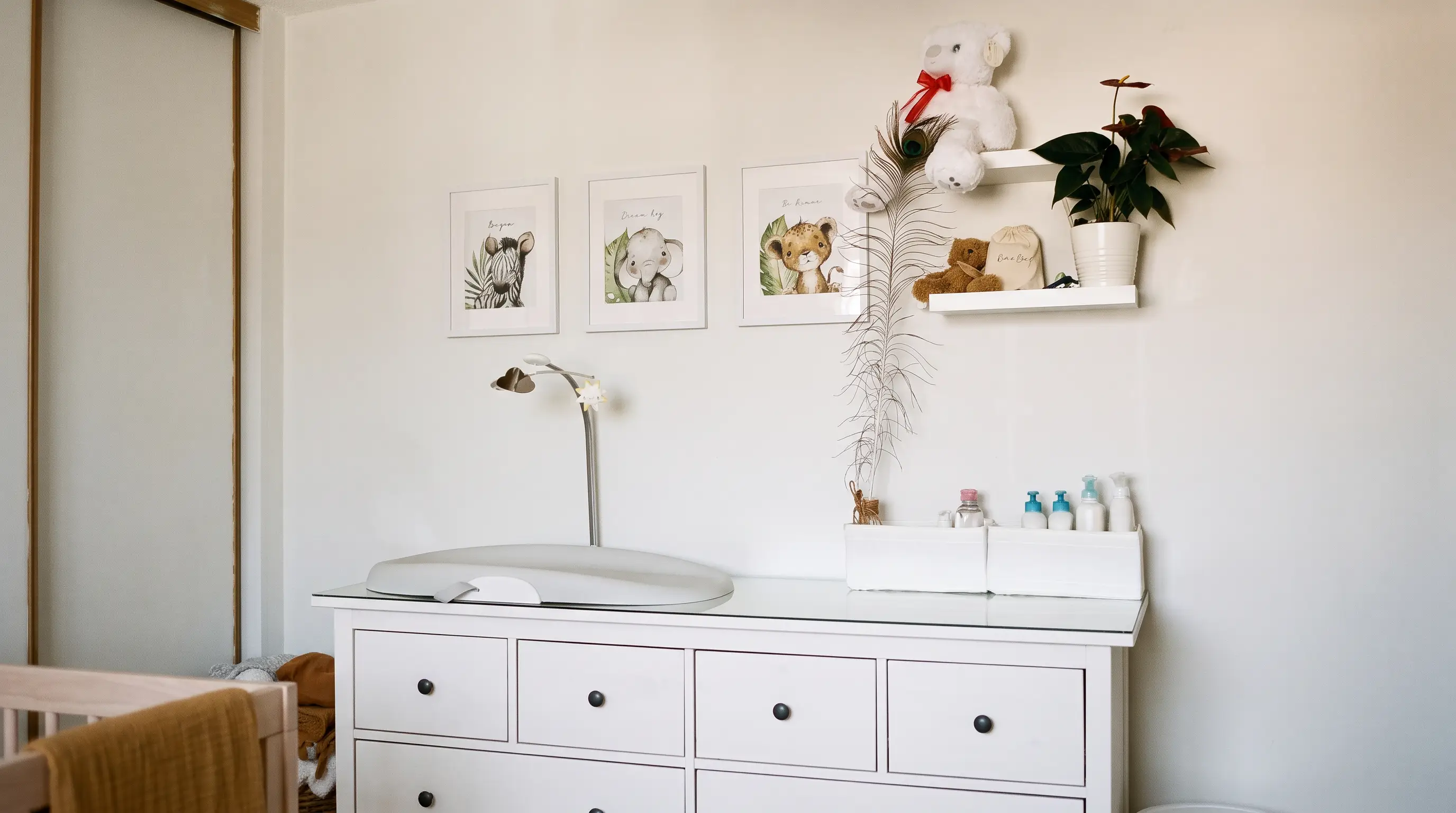 The white nursery dresser with a changing pad, three framed safari animal prints and shelves of keepsakes.